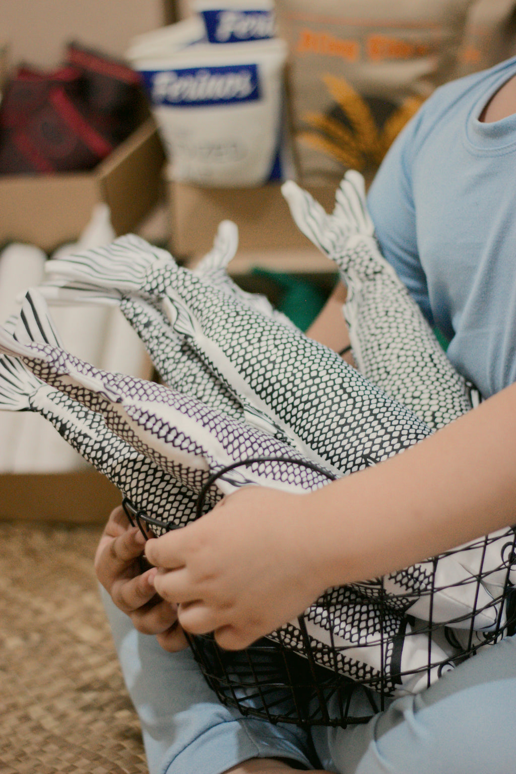 A person in a light blue shirt holds several white fish soft-toys with a black printed scales inside a black wire basket.